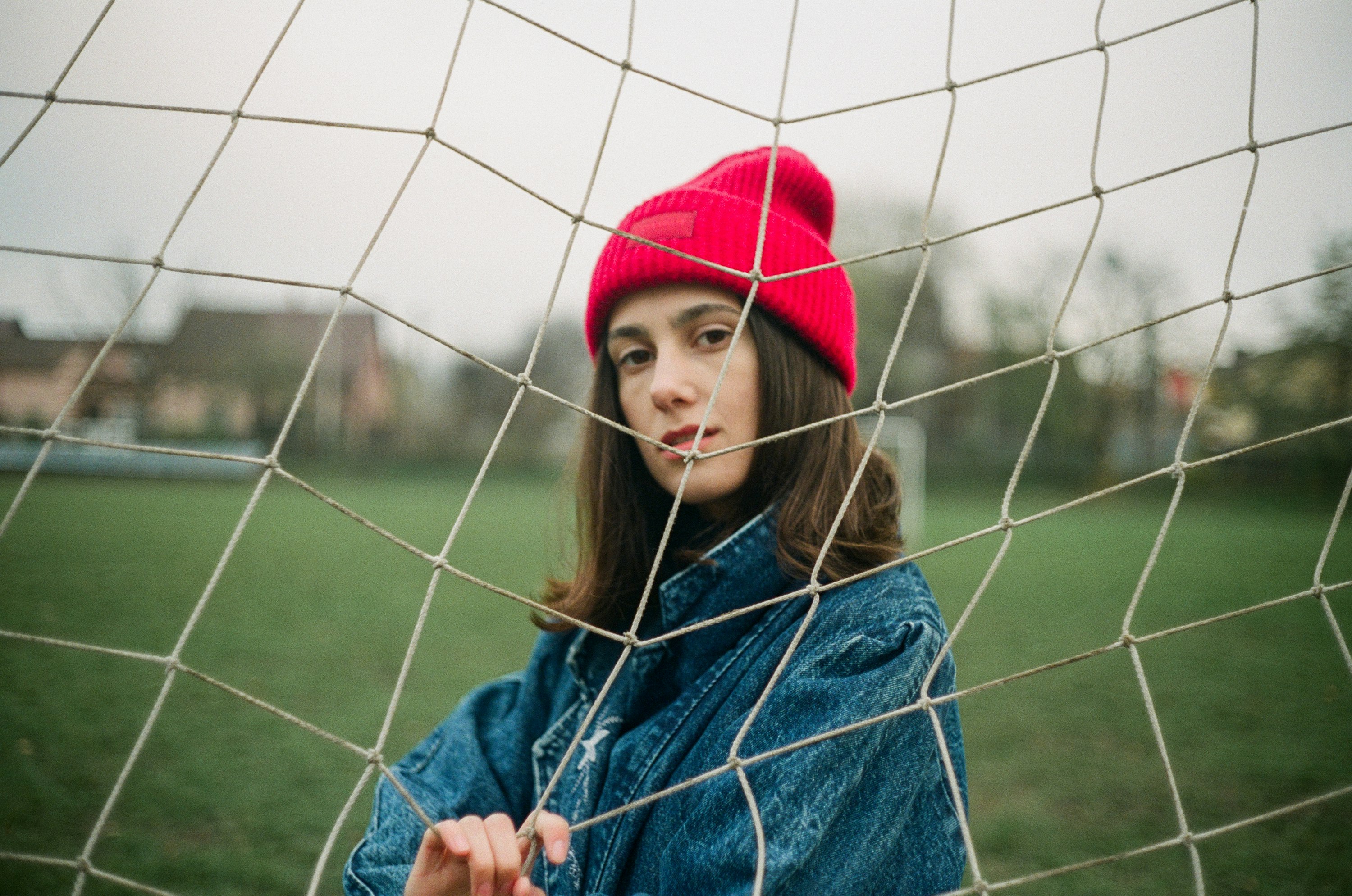 woman in blue denim jacket and red knit cap standing near gray metal fence during daytime